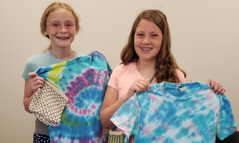 Two girls holding up the tie dye shirts they made