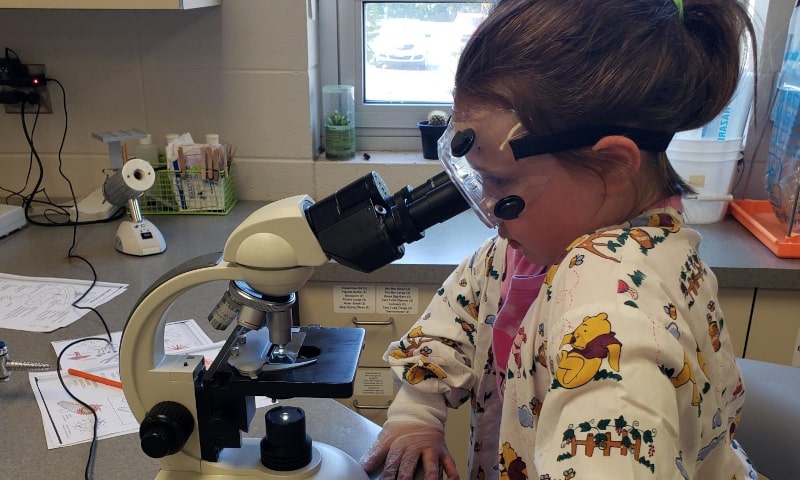 Girl with safety goggles looking into microscope