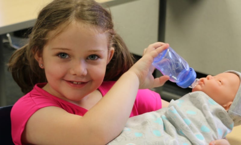 Girl feeding plastic baby with bottle