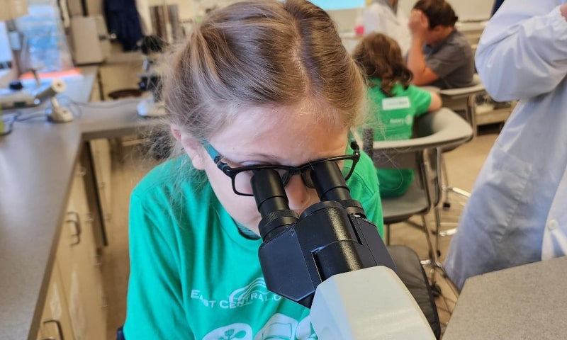 Girl in classroom looking into microscope