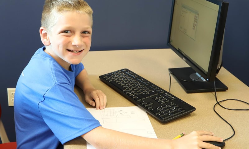 Boy smiling at the camera while working on a computer