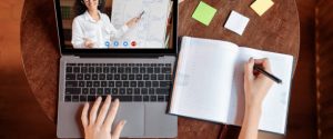 Distance Education Concept. Above top view of female student sitting at desk, writing in notebook, taking notes, using laptop, having online class with teacher. Remote studying from home, quarantine