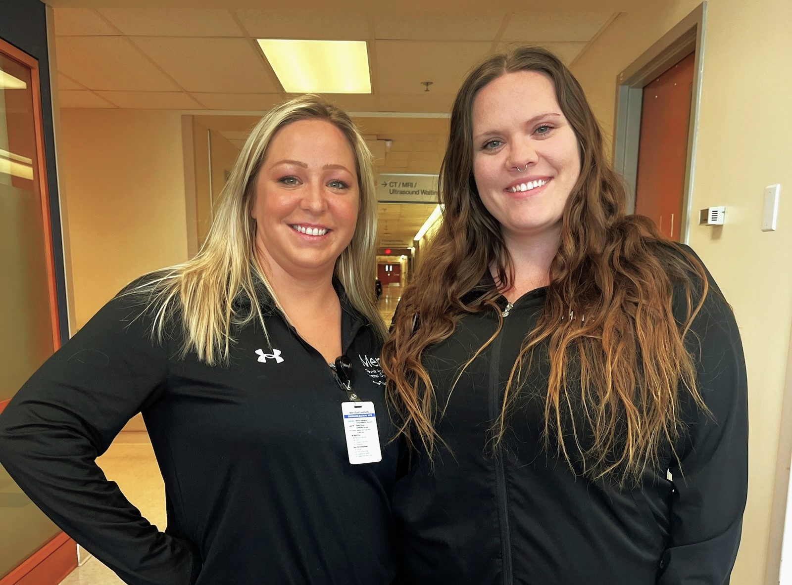 Two smiling ECC graduates in Mercy Hospital uniforms standign in a hallway at the Mercy South Trauma Center.