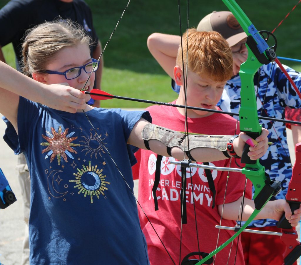 A boy and girl practicing archery outdoors during a Summer Learning Academy Archery class.