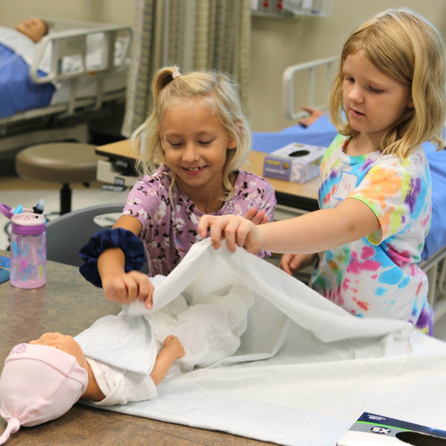 Two girls using a baby doll to learn about caring for babies in a college nursing lab.