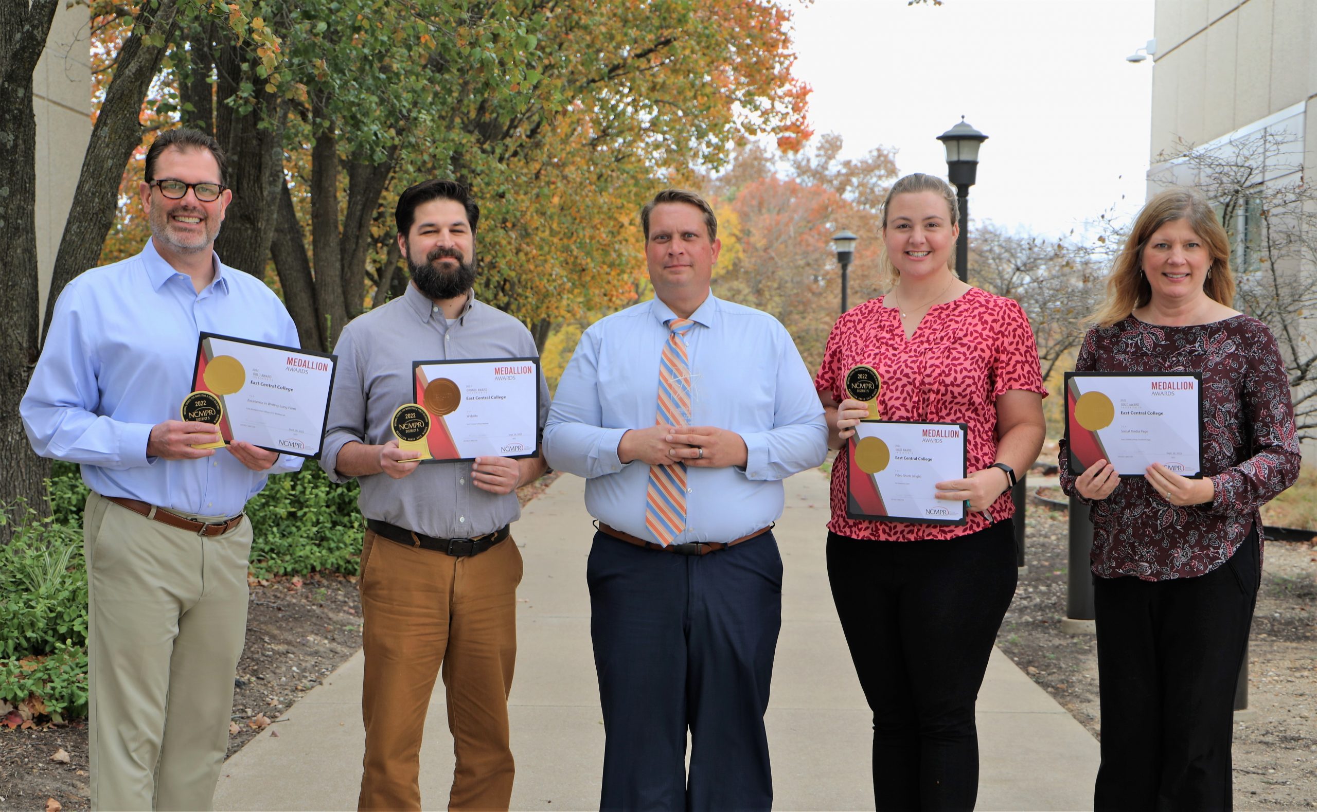 Group of professionals holding awards outdoors on a college campus