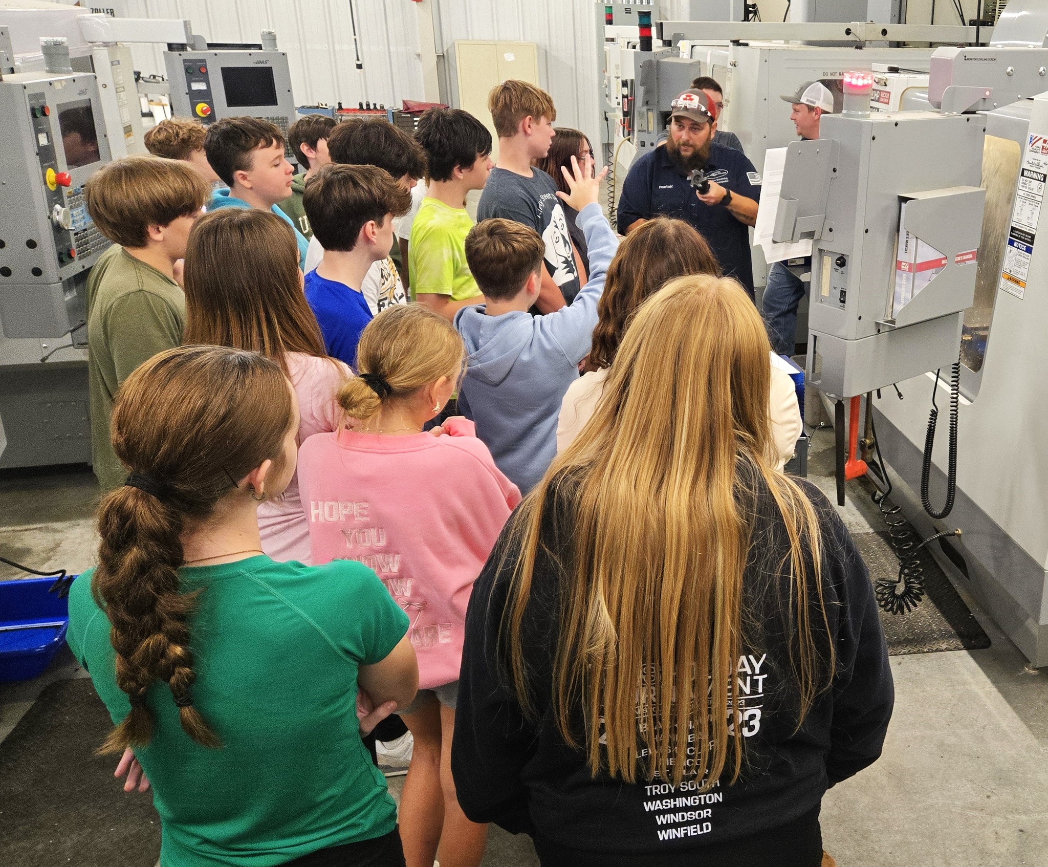 Group of middle school students around manufacturing equipment and instructor.