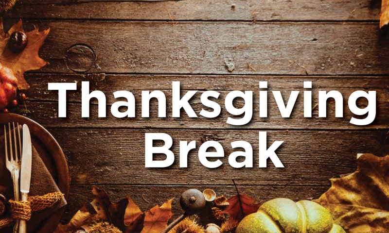 Leaves and pumpkin and plate with silverware on a wood tabletop with the text Thanksgiving Break