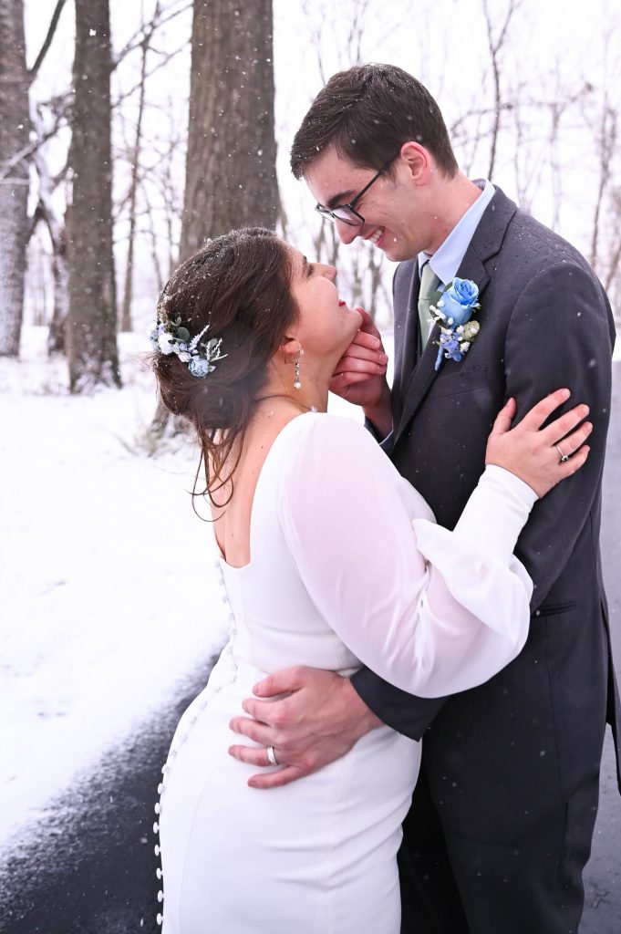 Male and female couple kissing outside in the snow following a wedding.